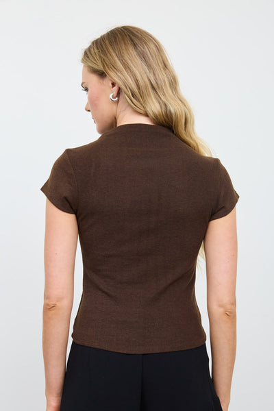 A woman shown from the back wearing a fitted short-sleeve brown top and dark pants against a plain light gray studio background.