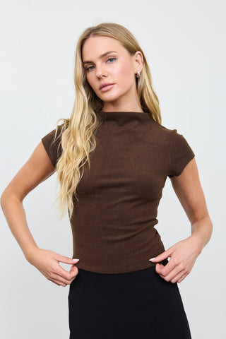 A blonde model wearing a fitted short-sleeve brown mock neck top and a black skirt, posing against a light gray studio background.