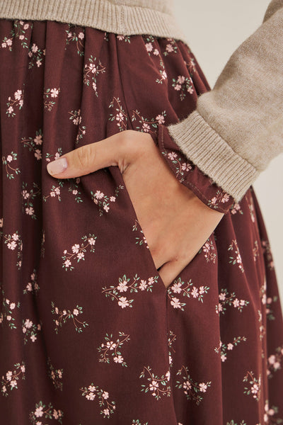 Close-up of a dark brown floral skirt with a hand in the pocket, styled with a beige knit sweater.