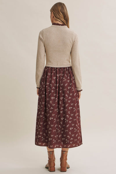 A woman shown from the back wearing a beige knit mock-neck sweater and a dark brown midi skirt with a white floral pattern, paired with brown leather boots, against a solid light beige studio background.