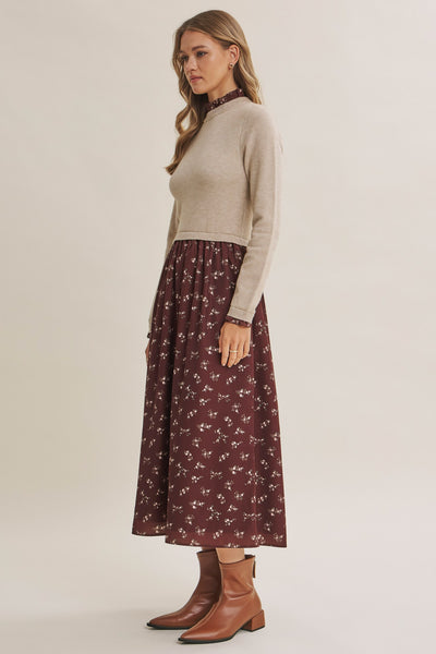 A woman modeling a two-piece outfit consisting of a beige mock-neck knit sweater and a dark red floral midi skirt, paired with brown leather ankle boots, against a plain light beige studio background.