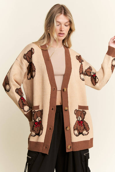 A woman wearing a beige cardigan with brown trim and teddy bear motifs, styled with a beige crop top and black cargo pants against a plain cream background.