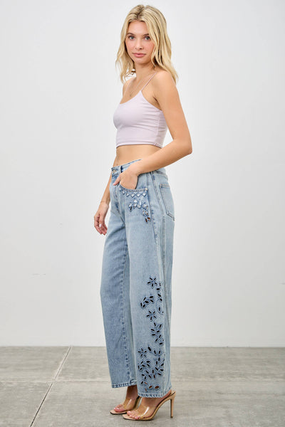 Woman wearing light blue jeans with floral embroidery and a pink top on a white background