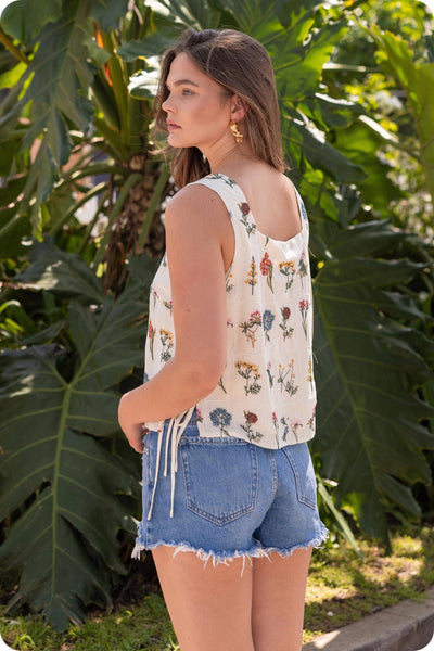 Woman wearing a floral sleeveless top and denim shorts standing in a garden.