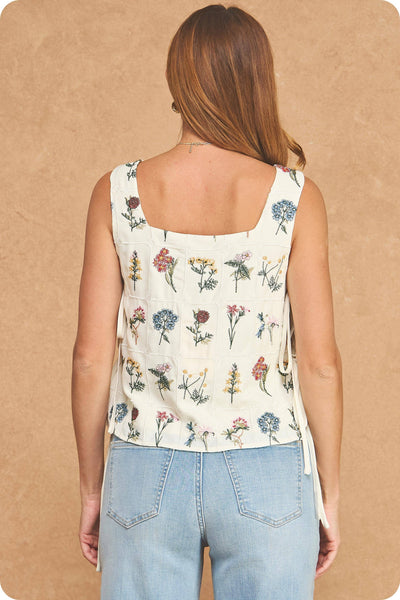 Woman wearing a floral sleeveless top and blue jeans on a beige background