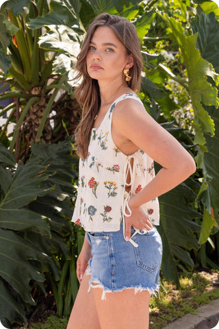Woman wearing a floral top and denim shorts standing in front of green foliage