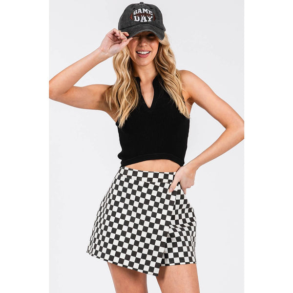 Woman wearing a black cap, black crop top, and checkered skirt on a white background