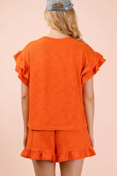 Person wearing an orange ruffled top and shorts set on a pink background