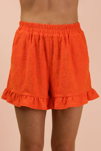 Orange shorts with ruffled hem on a beige background