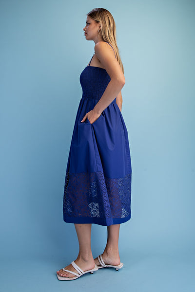 A woman modeling a strapless royal blue midi dress with lace detailing at the hem, standing against a solid light blue background.