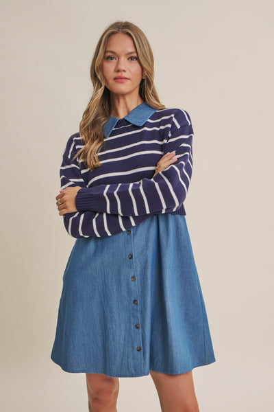 A woman modeling a long-sleeve knit polo sweater with navy and white horizontal stripes over a light blue collared shirt, paired with a blue denim button-front skirt, against a solid beige studio background.