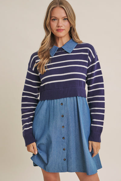 A woman modeling a color-block knit sweater dress with a navy and white striped yoke, a blue collar, and a blue denim-look button-front skirt against a plain beige studio background.