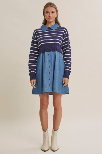 A woman modeling a color-block knit and denim dress with a navy and white striped sweater bodice, a light blue collar, and a blue denim skirt, paired with off-white ankle boots against a plain beige studio background.