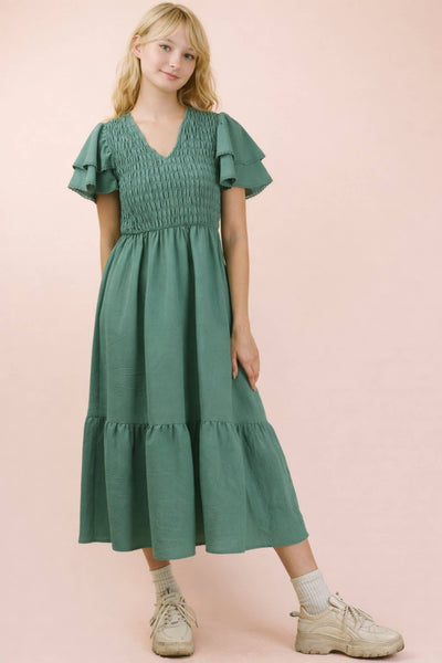 Woman wearing a green dress with ruffled sleeves against a pink background