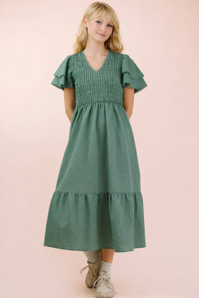 Woman wearing a green dress with ruffled sleeves on a pink background