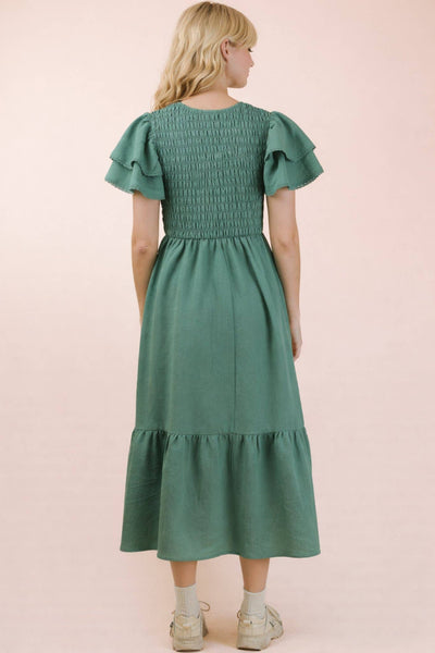 Woman wearing a green dress with ruffled sleeves and bottom hem on a pink background