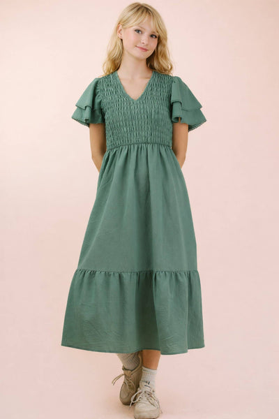 Woman wearing a green dress with ruffled sleeves on a pink background