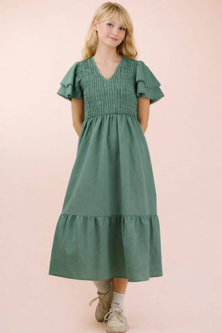Woman wearing a green dress with ruffled sleeves on a pink background