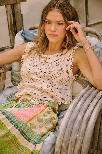 Woman sitting on a chair wearing a crochet top and patterned skirt.