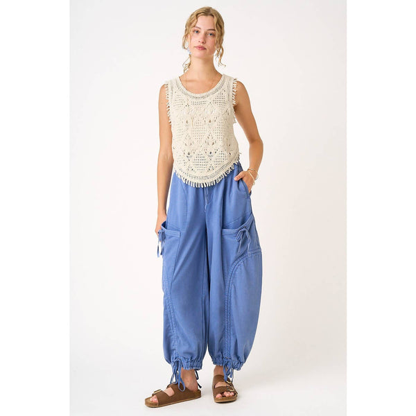 Woman wearing a sleeveless crochet top and blue harem pants on a white background