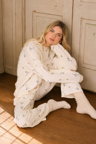 Woman wearing a white robe with a pattern, sitting on the floor in a sunlit room.