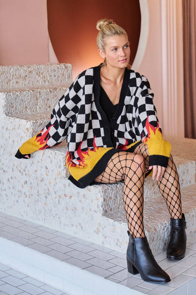 Woman wearing a checkered cardigan with yellow accents, black boots, and fishnet stockings sitting on steps.