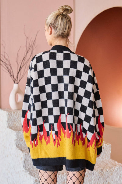 Person wearing a black and white checkered cardigan with flame patterns in a decorative setting.