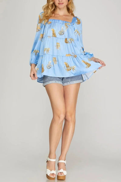 Woman wearing a blue blouse with animal print and denim shorts on a plain background