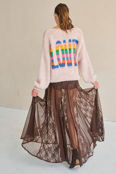 Person wearing a sweater with colorful letters and a lace skirt on a plain background