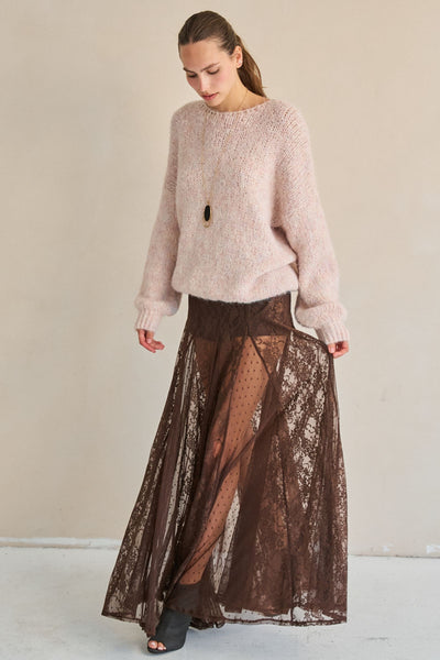 Woman wearing a light pink sweater and brown lace skirt against a plain background