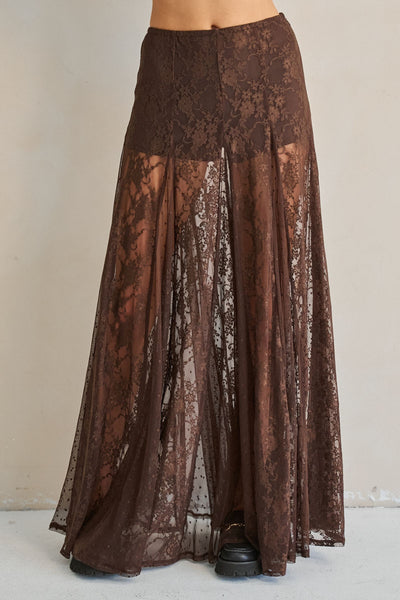A brown sheer lace maxi skirt with a solid brown waistband, shown on a model from the waist down against a neutral beige wall.