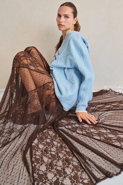 Woman wearing a light blue sweater and black lace dress against a neutral background