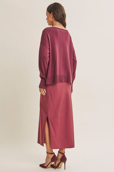 A woman shown from the back wearing a matching dusty rose long-sleeve knit top and midi skirt set, paired with matching heels, against a plain light beige studio background.