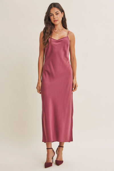 A woman modeling a satin slip dress in a dusty rose color, paired with matching heels, against a plain light beige studio background.