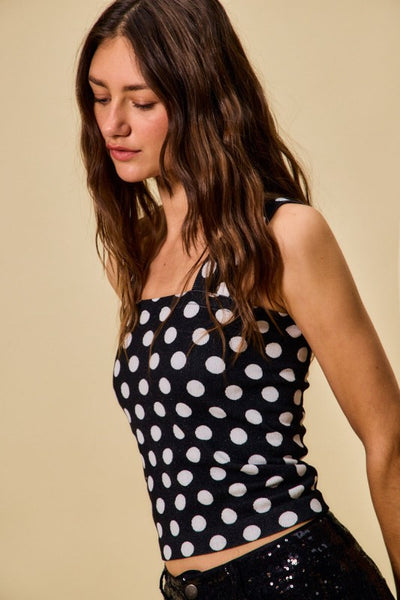 Woman wearing a black sleeveless top with white polka dots against a beige background