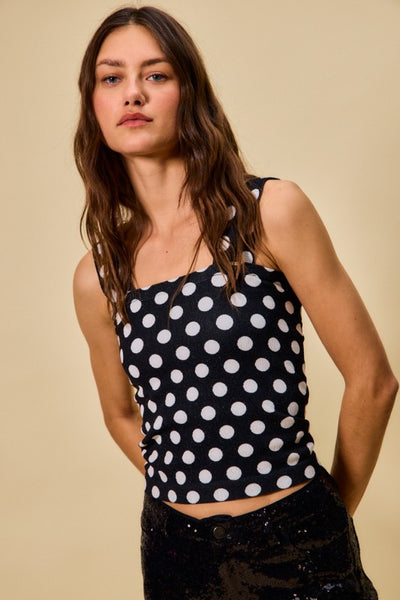 Woman wearing a black tank top with white polka dots against a beige background