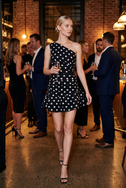 Woman in a black dress with white polka dots at a social event.