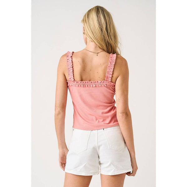 Woman wearing a pink tank top with ruffled straps and white shorts on a plain background