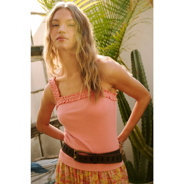 Woman wearing a pink top with ruffled straps in an outdoor setting with plants.