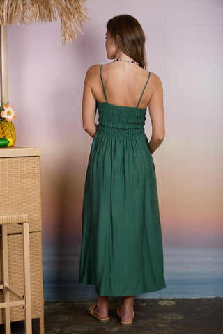Woman in a green dress standing by a wicker table with a blurred beach background