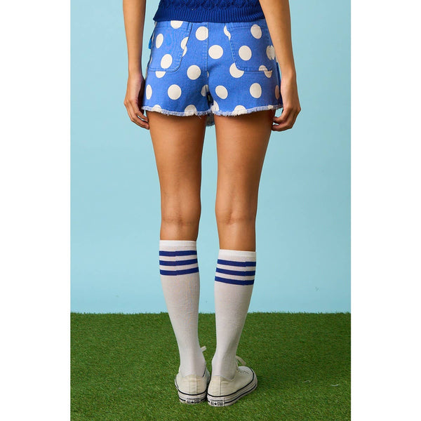 Person wearing blue polka dot shorts with white knee-high socks and white sneakers on a grassy field.