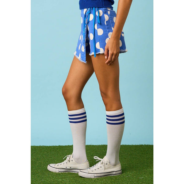 Person wearing blue shorts with white patterns, white knee-high socks with blue stripes, and white sneakers on a grassy background.
