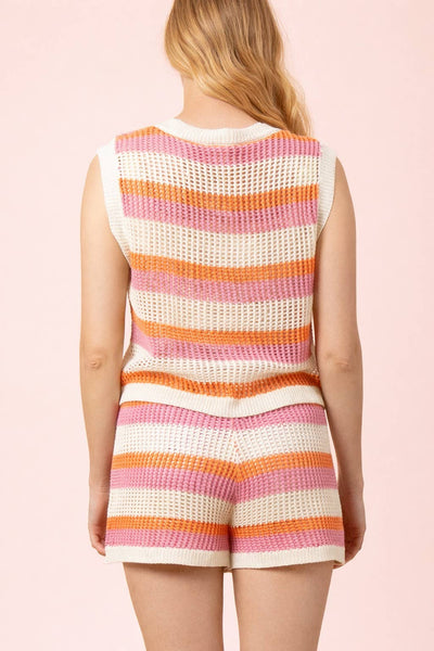 Woman wearing a colorful striped sleeveless top and shorts on a pink background