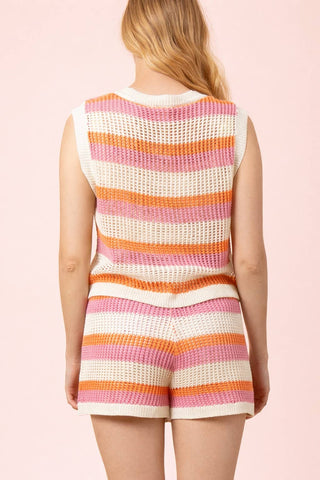 Woman wearing a colorful striped sleeveless top and shorts on a pink background