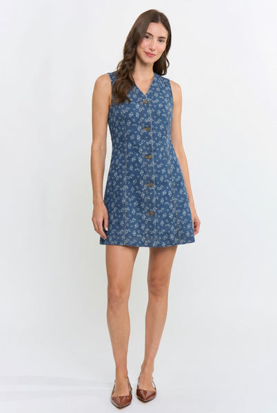 A woman modeling a sleeveless blue mini dress with a white floral pattern and a button-down front, standing against a plain white studio background.