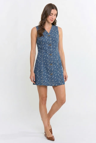 A woman modeling a sleeveless blue mini dress with a small floral pattern and a button-up front, set against a plain white studio background.