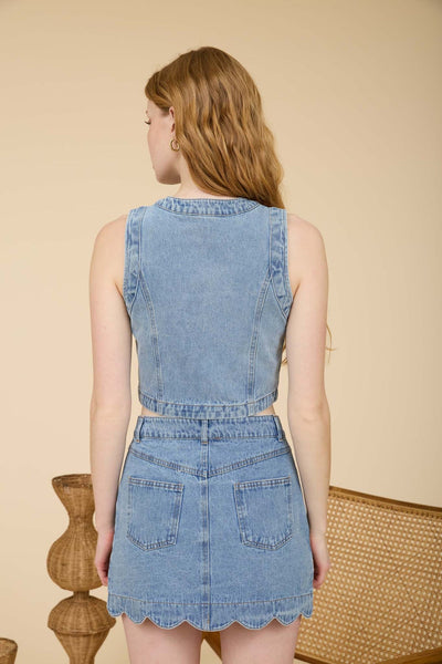 Woman wearing a sleeveless scalloped button-front denim vest top made from 100% cotton with a matching denim mini skirt.