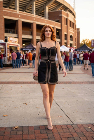 Woman in a black dress with gold accents walking outdoors near a stadium.