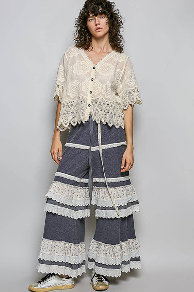 Woman wearing a lace top and wide-leg pants with a white background