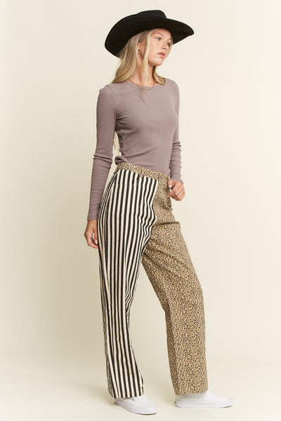 Woman wearing a mauve long-sleeve top and patterned pants with a black hat on a beige background